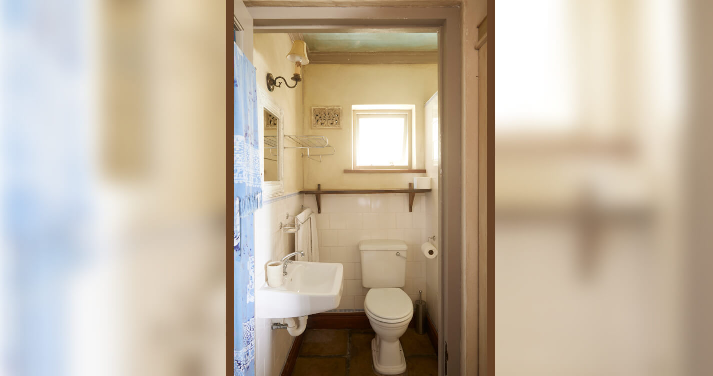 The Oyster Shell cottage’s quaint bathroom. It has soft beige walls and is naturally lit from sunshine through a small window.