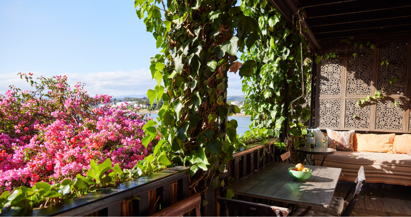 The Oyster Shell balcony dining area, with its daybed and sea view. A beautiful, pink flowering bougainvillea surrounds the balcony, romantically framing the view of the sea.