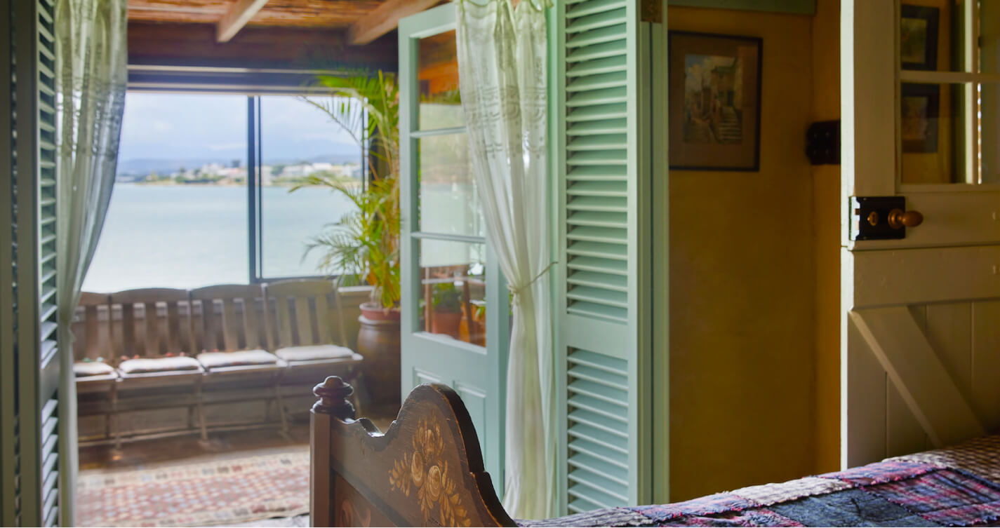 The sea view from the Robbins Nest bedroom. Open french doors allow natural light to fill the room. Beyond the doors is a blue framed window looking onto the sea.