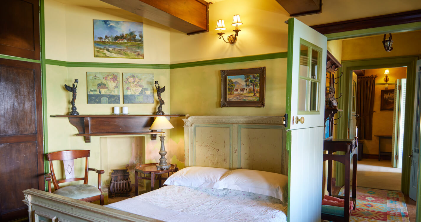 The Family Suite Seagull’s Nest bedroom. It has a double bed and walls painted in different shades of green. There is a fireplace against one wall. Artwork of landscapes hang throughout the room. Two angels stand on the mantle above the fireplace.