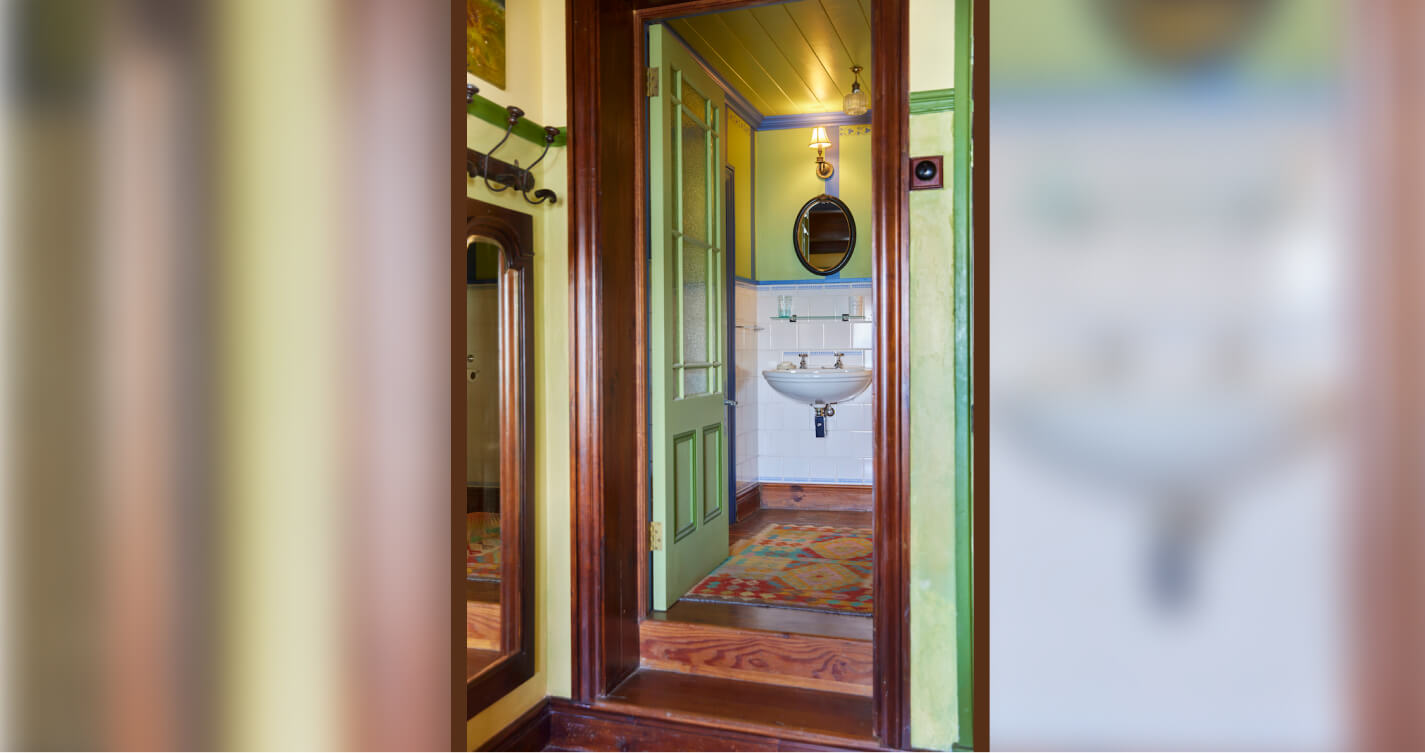 The Seagulls Nest en-suite bathroom. It is painted in greens and blues. A decorative rug runs the length of the wooden floor. A mirror hangs above the basin.