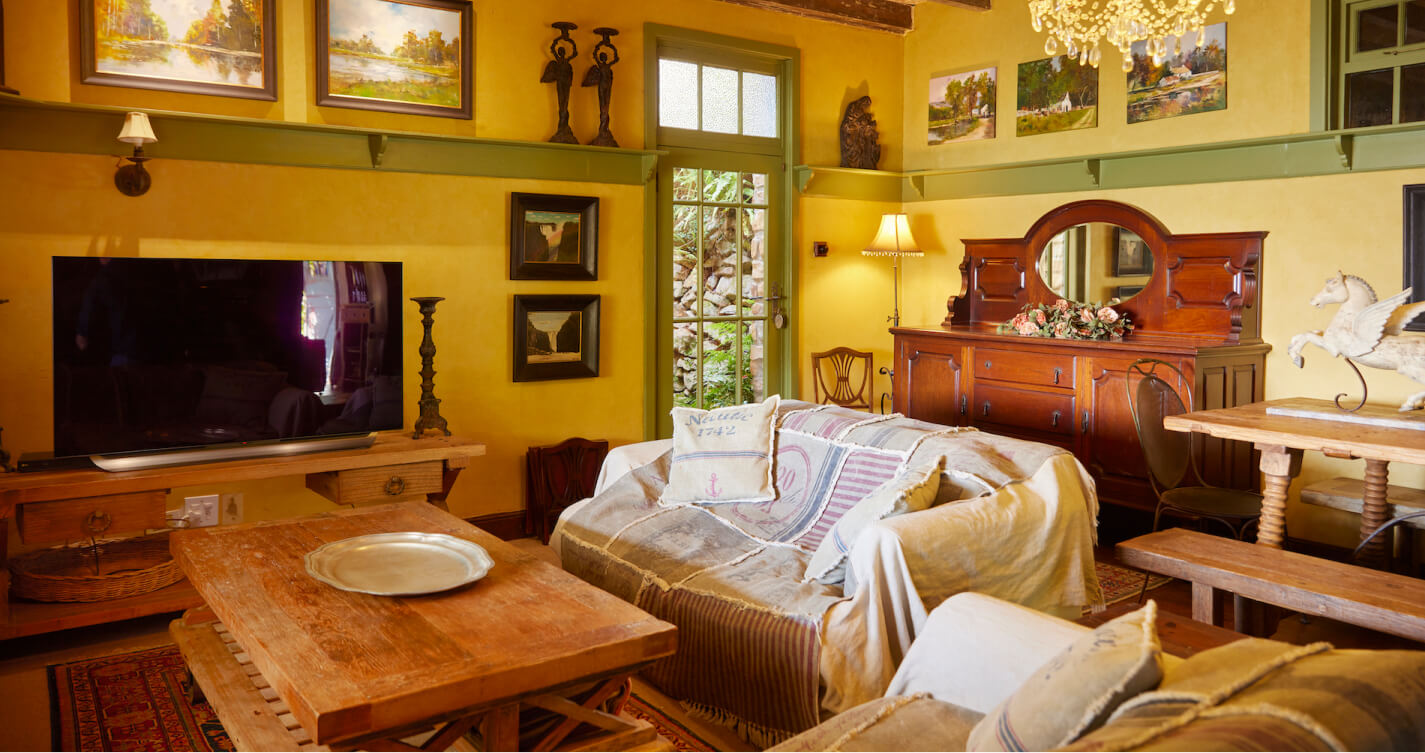 The Luxury Suite TV room. A smart TV is surrounded by big, comfortable looking couches. The surrounding room is decorated with landscape paintings, sculptures and a crystal chandelier.