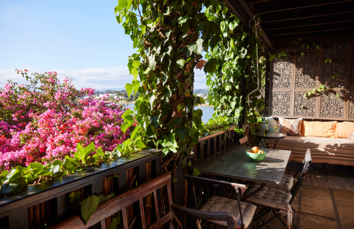 The Oyster Shell balcony dining area, with its daybed and sea view. A beautiful, pink flowering bougainvillea surrounds the balcony, romantically framing the view of the sea.